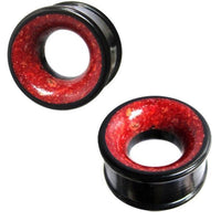 Load image into Gallery viewer, Two black Holztunnel Eisenholz gauges with red Koralleninlay are shown against a white background. The hand-carved wooden plugs feature flared edges, a hollow center, and a tribal-inspired design.
