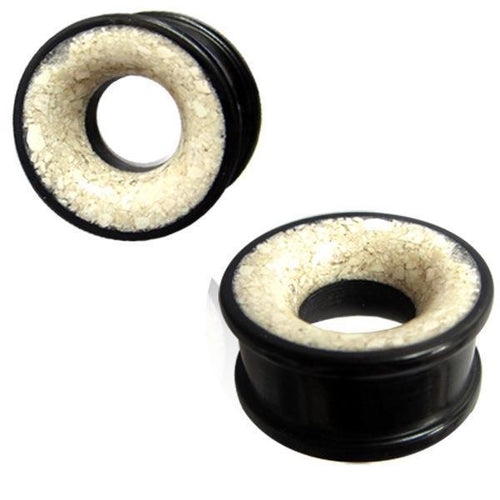 Two black, circular Eisenholz Tribal Plugs with a white Marmor inlay are shown against a white background—one Holztunnel is viewed from the side, the other at an angle. Hand-carved Tunnel schwarz Marmorinlay weiß Expander.
