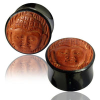 Cargar imagen en el visor de la galería, Two Horn Plug Buddha schwarz braun Flesh Tunnel plugs with round wood inlays and carved Buddha design are shown on a white surface, each reflected below.
