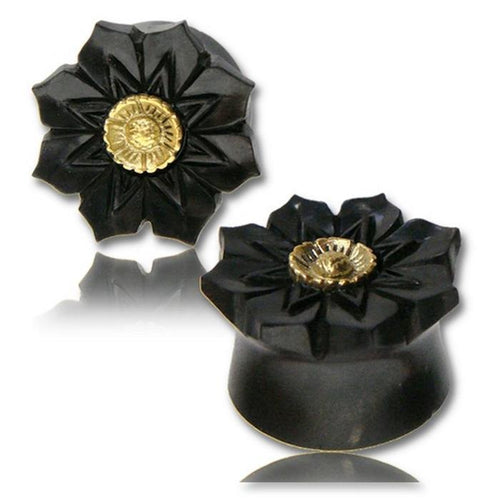 Two black Tamarinden Holz Plugs with antique gold, nickel-free brass inlay featuring a lotus flower design are displayed on a white background with a slight reflection.