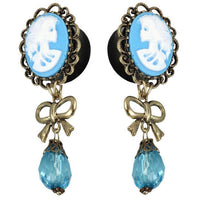 Load image into Gallery viewer, Vintage-style earrings: blue and white acrylic cameo skeleton woman, gold brass border, bow accent, faceted blue glass teardrop pendants—Plug Piercing.
