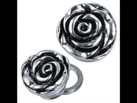 Load image into Gallery viewer, Two metallic, silver-tone Edelstahl Schraub Plug Tunnel Plugs, rose-shaped with dark oxidized detailing. One lies flat while the other is tilted to show a circular back opening and layered, textured petals for a plastic, dimensional effect.
