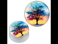 Cargar imagen en el visor de la galería, Two round white acrylic plugs feature a black tree silhouette against a colorful sunset in blue, pink, orange, and yellow. These glossy Piercing Plugs are called &quot;Plug weiß Acryl Baum schwarz Sonnenuntergang bunt Ohrschmuck.
