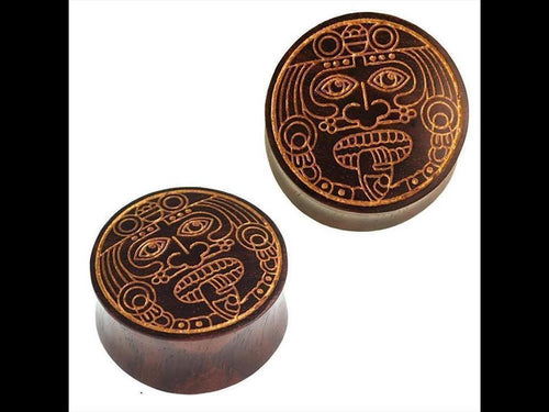 Two round, dark brown Holz Plugs by Sonoholz with golden engraved designs of a warrior mask face. Featuring detailed eyes, nose, mouth, and a tongue for an authentic look.