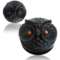Cargar imagen en el visor de la galería, A round, black hand-carved Holz Plug Eule with a lid shaped like an owl’s face, featuring textured feathers and brown eyes, is shown from two angles on a white background.

