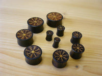 Cargar imagen en el visor de la galería, Nine Plug Arangholz Wikinger Kompass Inlay double flared plugs of various sizes, featuring rune-inspired circular carvings, are displayed on a light wood surface, each piece showcasing a decorative, mystical Norse design.
