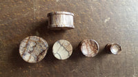 Load image into Gallery viewer, Five Tribal Tigerholz konkav Maserung Holz Plugs, hand-carved and ribbed, are arranged from largest to smallest on a brown wood surface, displaying earthy tones and distinctive grain patterns.
