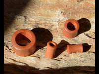 Load image into Gallery viewer, A finely grained, convex, red-brown wooden tunnel (Holz Tunnel rot braun fein gemasert konvex Rosenholz) is displayed on a textured wooden surface, casting distinct shadows in bright sunlight.
