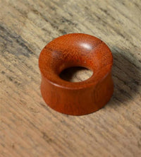 Load image into Gallery viewer, A handmade Blutholz Fleisch Tunnel rötlich, double flared and round with a wide center hole, rests on a textured, light-colored wooden surface.
