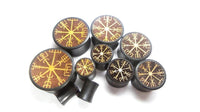 Cargar imagen en el visor de la galería, Seven round, black Plug Arangholz Wikinger Kompass Inlay double flared plugs with brown tops feature gold Vegvisir rune designs on a white background. One plug is tipped forward, revealing its side profile.
