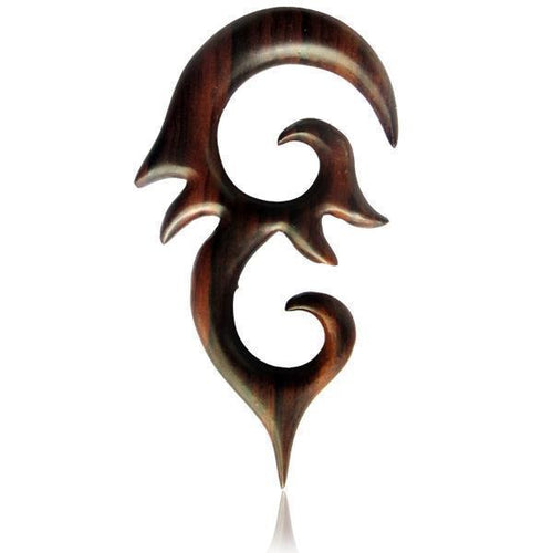 The Sonoholz lang Tribal Piercing features hand-carved, dark wood with pointed ornament and swirling curves. This unisex, organic expander displays a sharp, tribal-inspired design, shown against a white background.