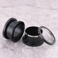Load image into Gallery viewer, Two Metalltunnel Tunnel Chirurgenstahl Unisex Edelstahl Plug schwarz Rand Expander Piercings—one assembled, the other unscrewed into three parts—are shown on a light gray textured surface.
