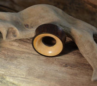 Load image into Gallery viewer, A smooth, round Holz Tunnel braun gelb aus Sonoholz (Teakholz), double flared, with a dark brown exterior and light beige interior, rests on driftwood—perfect as natürlicher Piercing-Schmuck.
