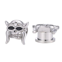 Load image into Gallery viewer, Two silberfarbenen Edelstahl Plugs, inspiriert vom Totenkopf Wikinger Helm Design, zeigen filigrane Details: einer frontal mit Hörnern und schwarzen Augenhöhlen, der andere seitlich und von hinten. Modell: Edelstahl Plug silber Farben Totenkopf Wikinger Helm.
