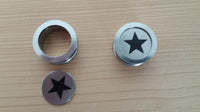Load image into Gallery viewer, Two round Edelstahl Tunnel Plug Schraubplug Stern schwarz silber with star cutouts rest on light wood; one is disassembled to show the Stern insert, the other is assembled, highlighting the Schraubverschluss and ribbed piercing design.
