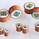 Load image into Gallery viewer, Small wooden spools, inspired by the Organic Sabaholz Plug Paua Abalone design, feature tiny bird and fish images with white tops and are arranged in groups on a white surface.
