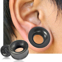 Load image into Gallery viewer, A close-up of an ear with an Eisenholz Tunnel schwarz fein gemasert Holztunnel Plug inserted into a stretched lobe; two more handgeschnitzte Tribal Holz Plugs are shown in the lower left corner.
