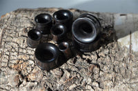 Load image into Gallery viewer, A selection of Eisenholz Tunnel schwarz fein gemasert Holztunnel handgeschnitzt Tribal Holz Plug Expanders in different sizes is displayed on textured wood, with light accentuating the tunnels&#39; fine grain and the wood&#39;s natural details.
