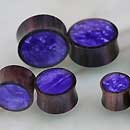 Load image into Gallery viewer, Four pairs of Holz Plug Sonoholz lila schillernd Resin Inlay double flared plugs, each with round, metallic edges and shimmering purple centers, are displayed on a light surface in a loose cluster, showing different sizes.
