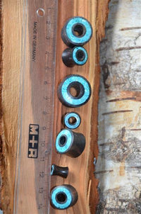 Cargar imagen en el visor de la galería, A clear M+R ruler marked Made in Germany lies on wood beside seven Flesh Tunnel Eisenholz schwarz Rim Crushed Türkis Inlay, arranged largest to smallest. A tree trunk appears in the background.
