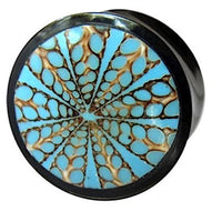 Cargar imagen en el visor de la galería, The Horn Plug Spinnennetz blau is a round black plug hand-carved from Büffelhorn, featuring a blue and brown geometric starburst pattern on its face.
