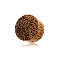 Load image into Gallery viewer, A handmade hell Holz Plug Punkte Muster Kokosholz features a round, tan-brown design with dark spots on its flat surface and reddish side streaks, shown against a white background with a subtle reflection below.
