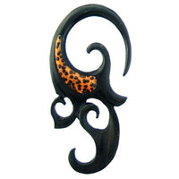 Load image into Gallery viewer, A decorative black Holz Piercing Eizenholz Spirale features curved tribal shapes and an orange-brown spotted Kokosholz Inlay accent on one side.

