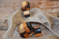 Load image into Gallery viewer, Three laminiert Holzplug vier Farben Muster Tribal Holz Plug are displayed on a curved driftwood, highlighting their double flared style and handmade craftsmanship in natural wood tones against a rustic background.
