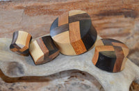 Load image into Gallery viewer, Four laminiert Holzplug vier Farben Muster Tribal Holz Plugs, each handmade with interlocking dark and light wood patterns, are arranged on textured driftwood, set against a blurred wooden background.
