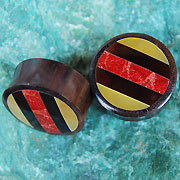 Load image into Gallery viewer, Two circular Holz Plug Tamarindenholz Resin Perlmutt Koralle Streifen Tunnel Tribal Expander plugs with dark brown sides and striped tops in red, yellow, and black rest on a green textured surface.
